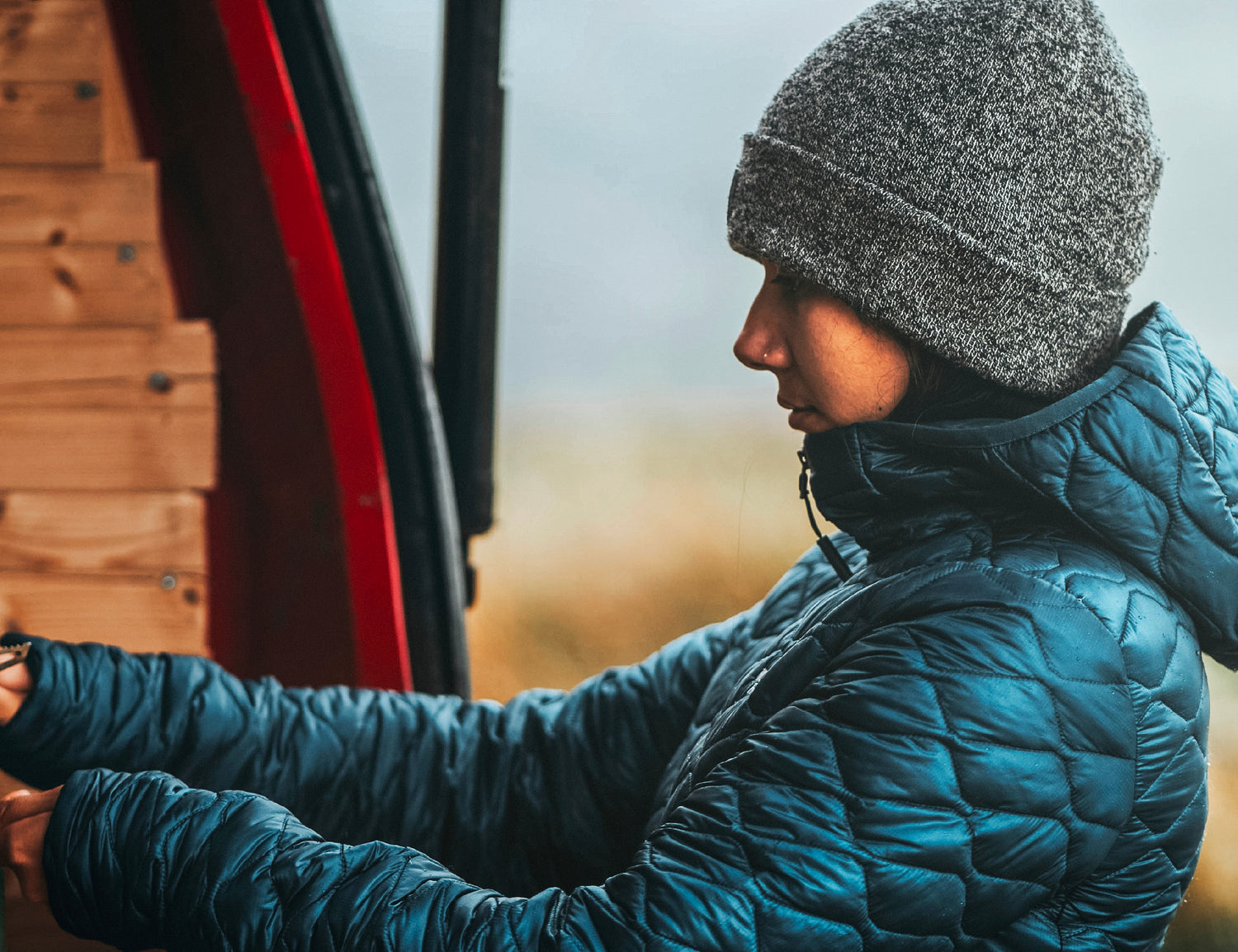 Female traveller bundled in outerwear as she prepares a warm drink in the rear of her camper van