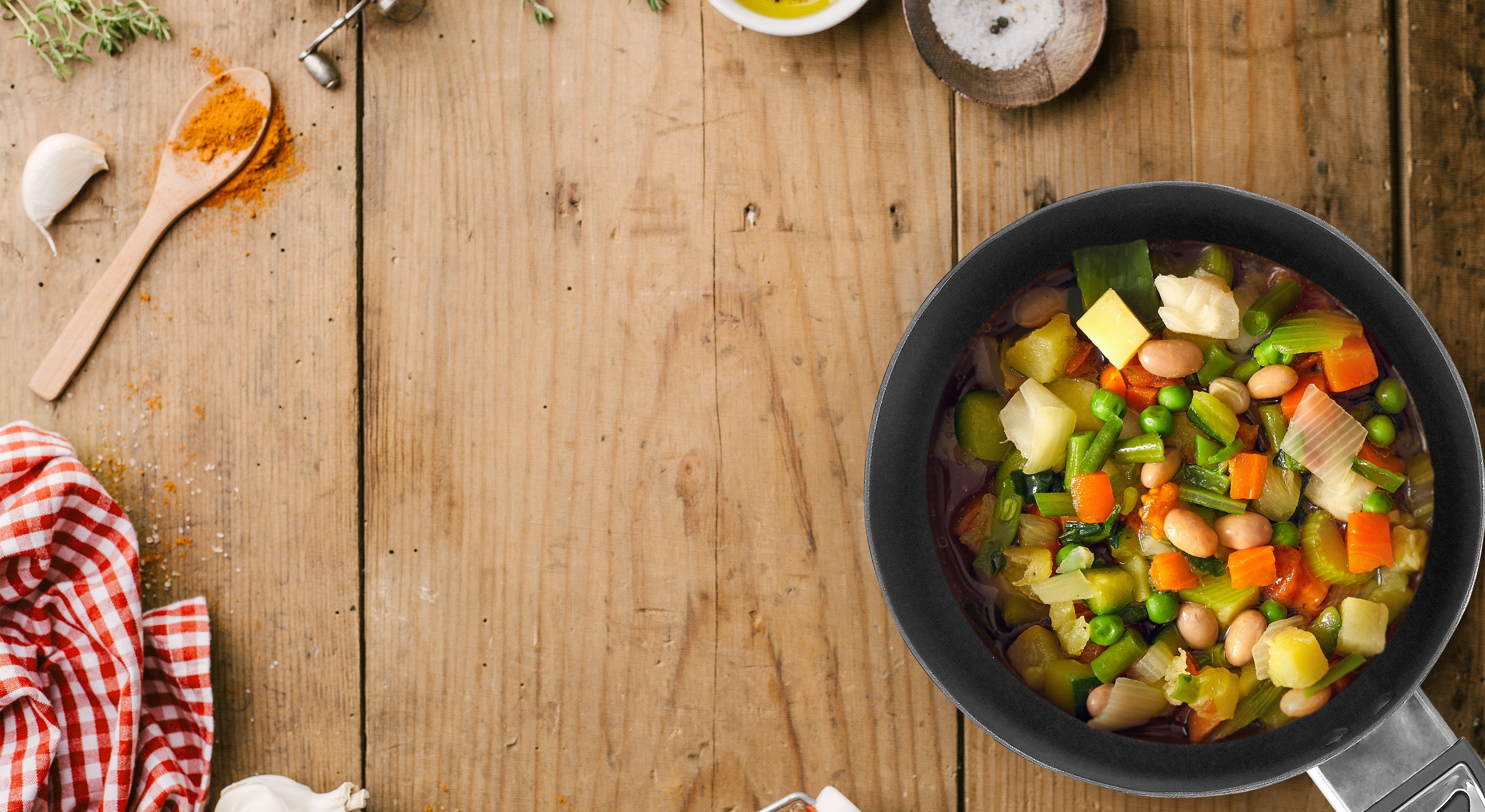 12 Volt Cooking Pan filled with a cooked veggie stew sitting atop a wooden table with utensils, napkins, and spices nearby