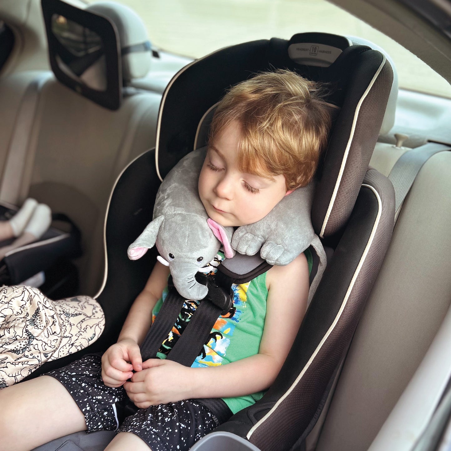 A youngster wears one of the Kids' Junior Travel Pillows around their neck while sleeping in their car seat in the rear of a vehicle.