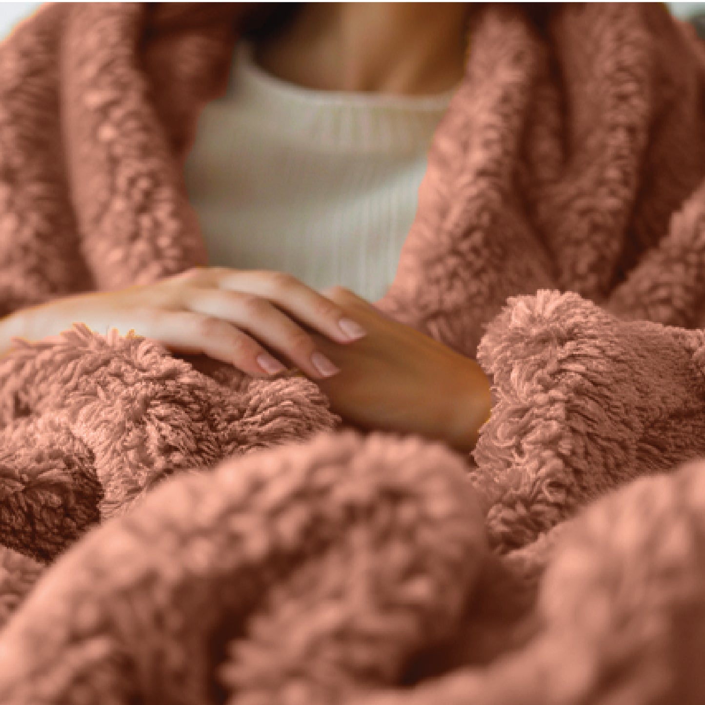 A person's hands rest softly on a coral Travel Time Sherpa Teddy Throw Blanket. Dressed in a white sweater, they embody warmth and comfort.