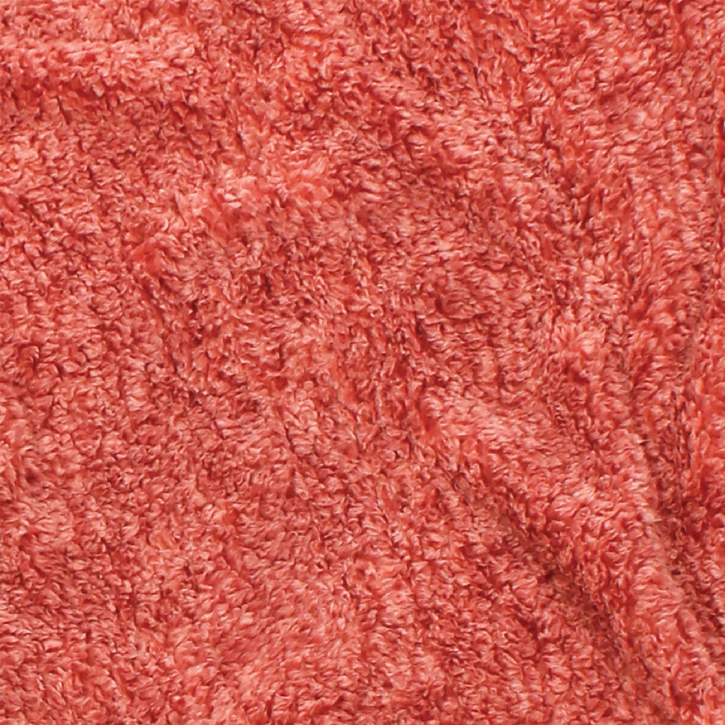 A close-up of the blanket's textured coral, salmon-colored fabric that has a soft, fluffy appearance. This machine-washable material exhibits subtle shading variations, adding depth and a cozy, inviting look.