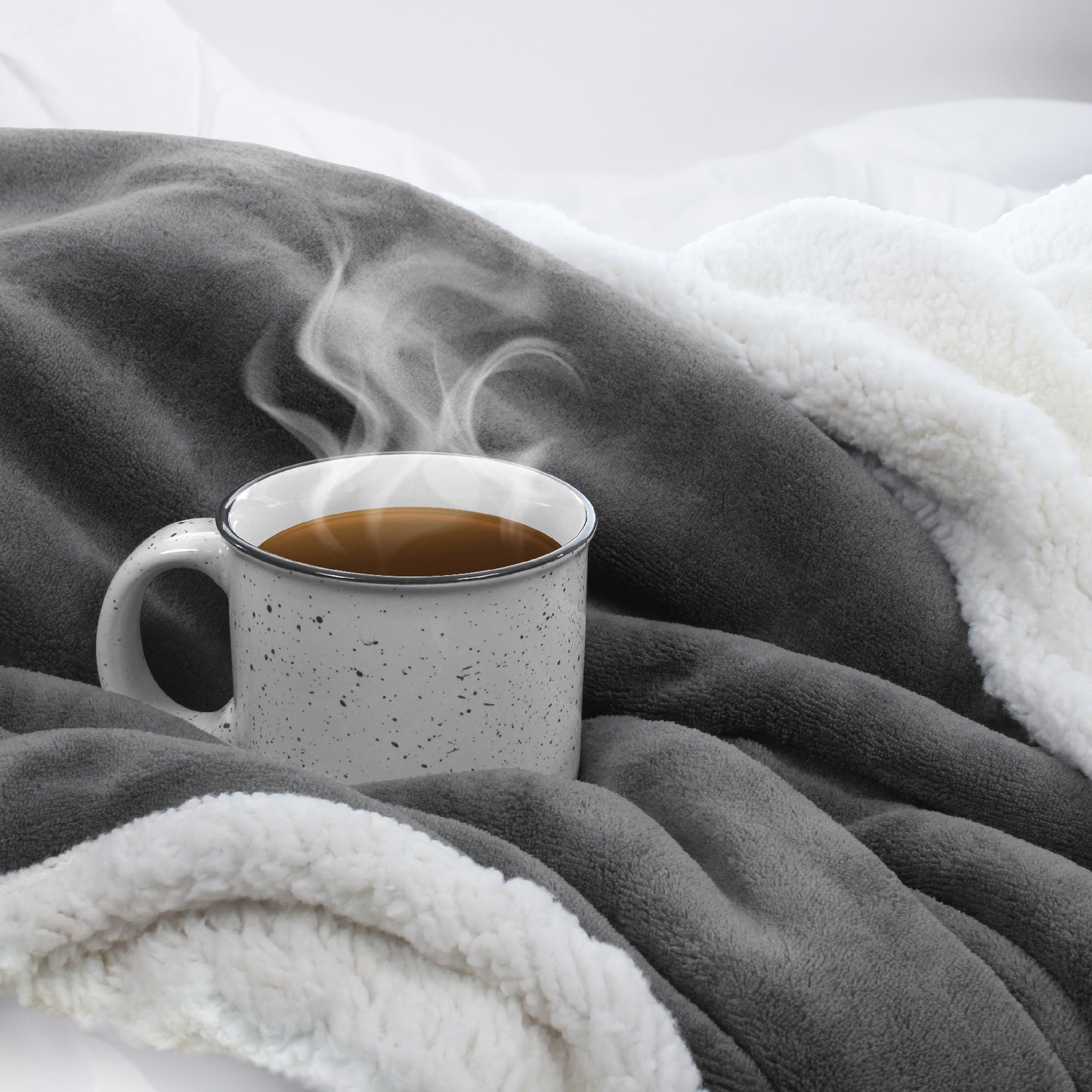 A steaming cup of coffee nestled into the ultra-cozy and soft dark gray Sherpa Fleece Reversible Throw Blanket.