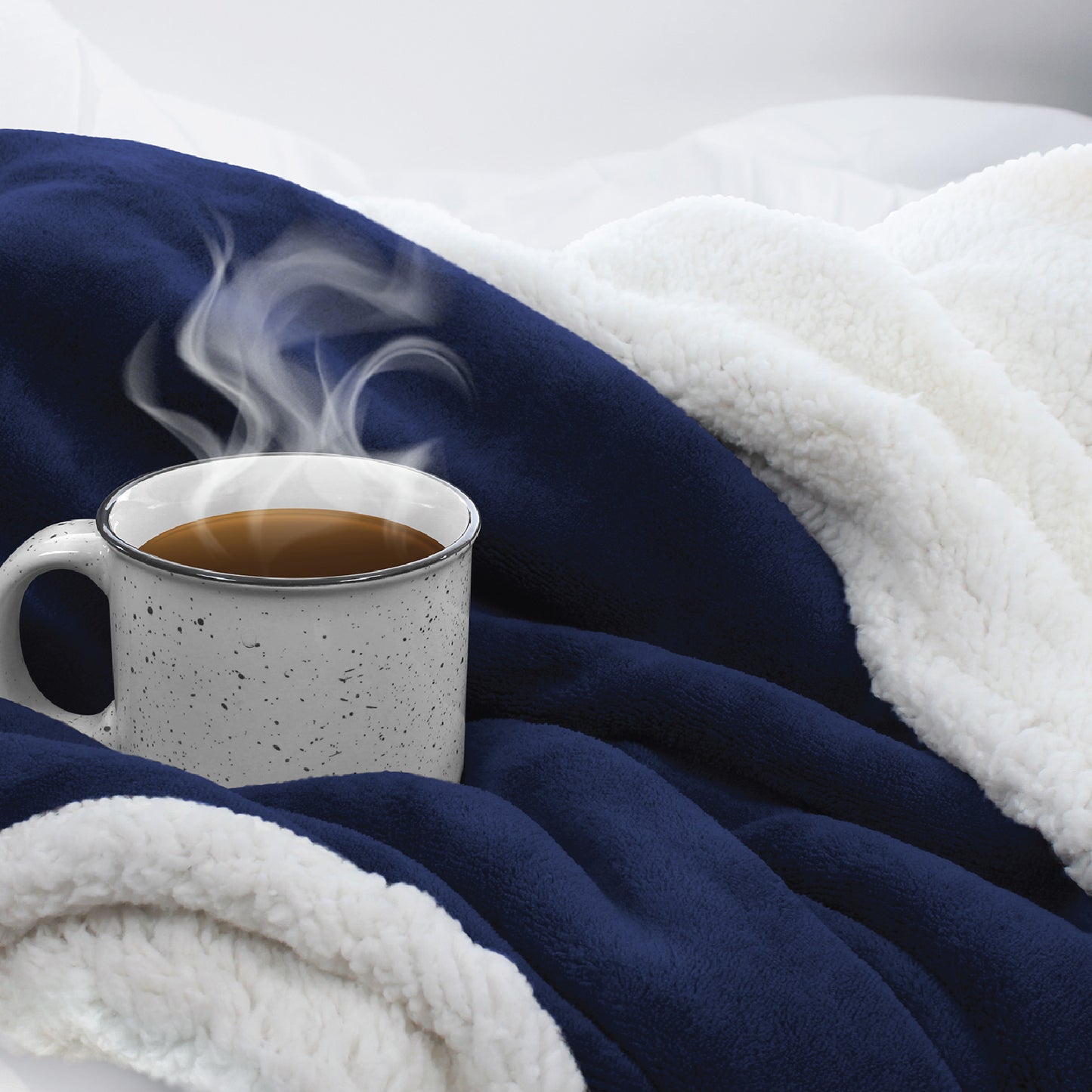 A steaming cup of coffee nestled into the ultra-cozy and soft navy Sherpa Fleece Reversible Throw Blanket.