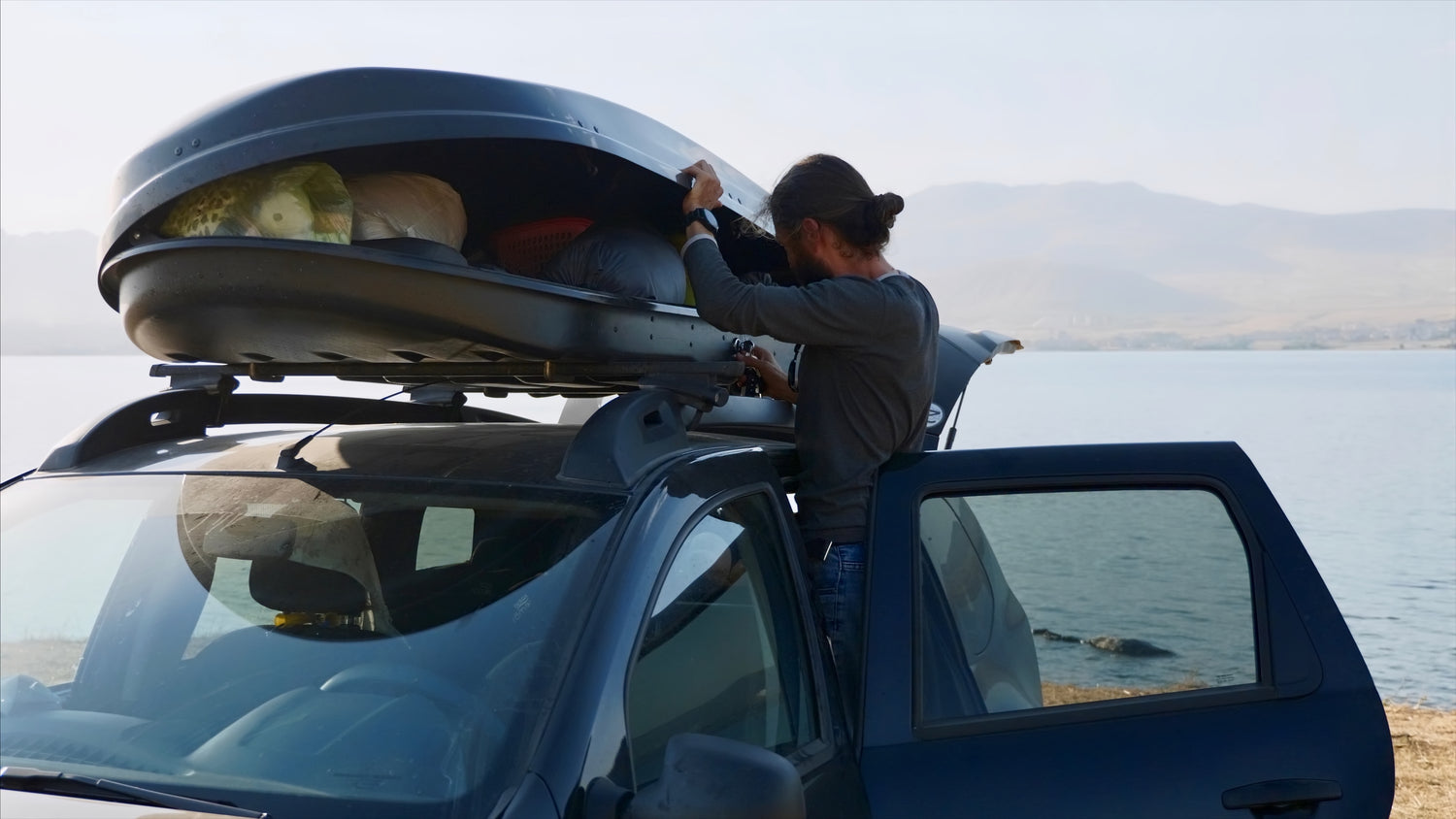 Active traveller packing up a car top storage container with his car door open, soon to be heading out on his next adventure