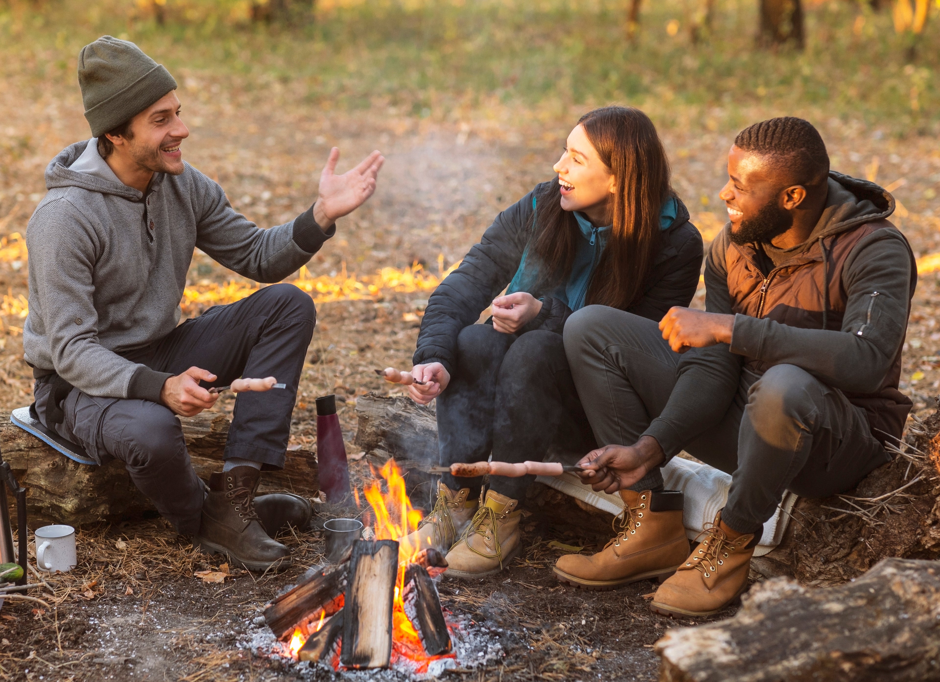 A group of travelers seated in front of a campsite fire using Travel Time cookware to prepare a warm meal