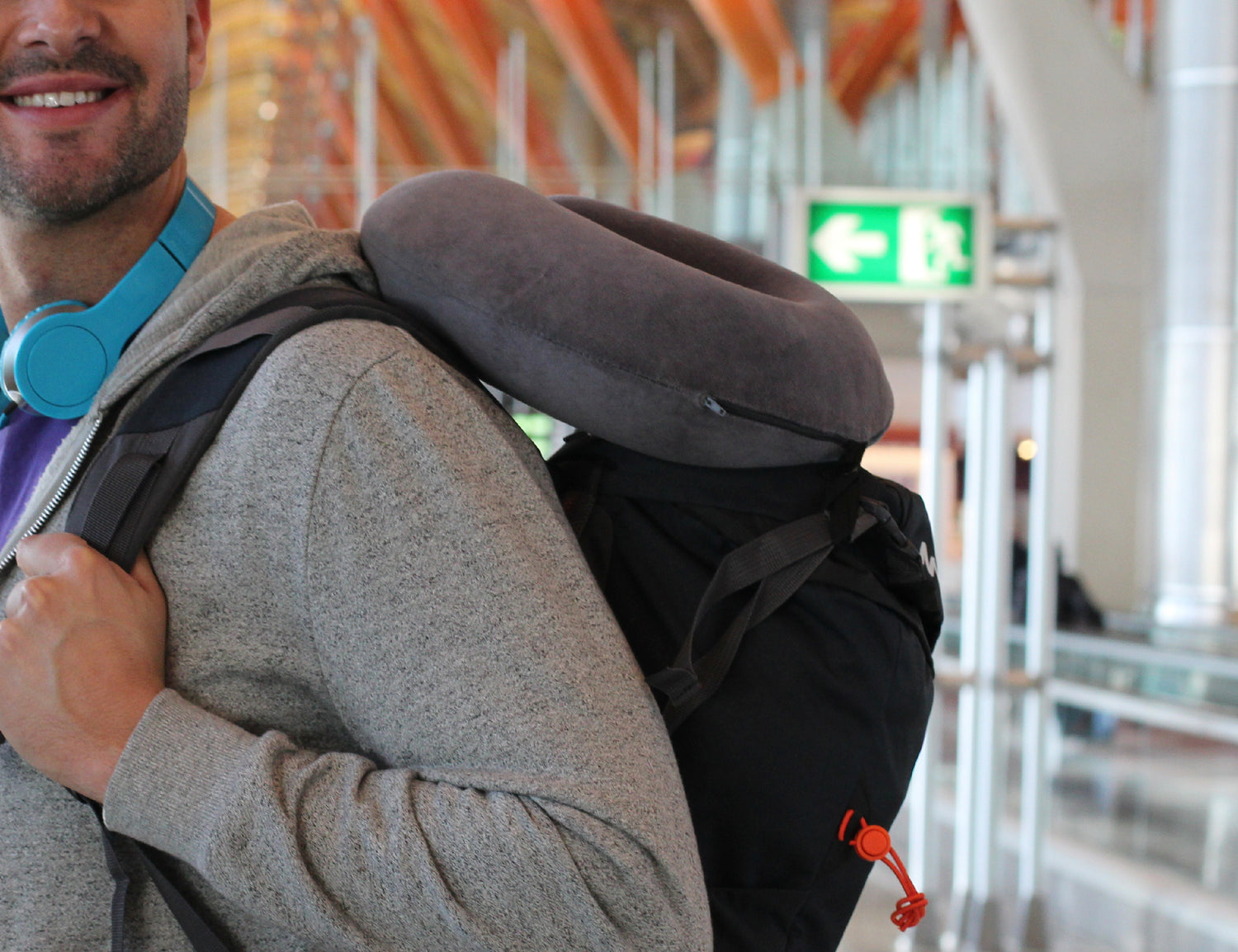 Traveller sporting a carry-on backpack with a Plush Travel Neck Pillow attached to it as they move throughout an airport