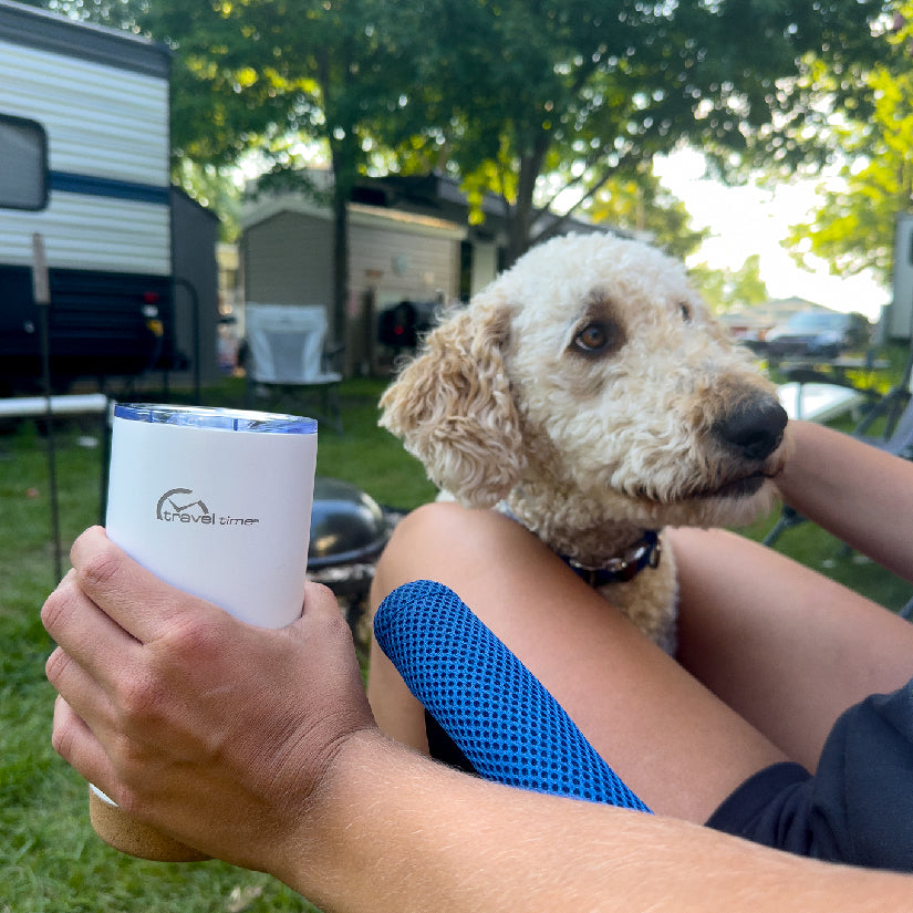 Stainless Steel Travel Tumbler 20oz in white held in the hand of a person hanging out outside their RV camper with their dog