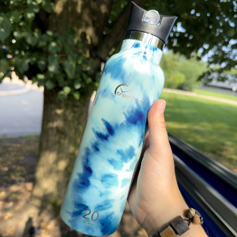 Stainless Steel Water Bottle with Flip Straw 20oz held in hand of someone who is outside camping in nature in front of a tree