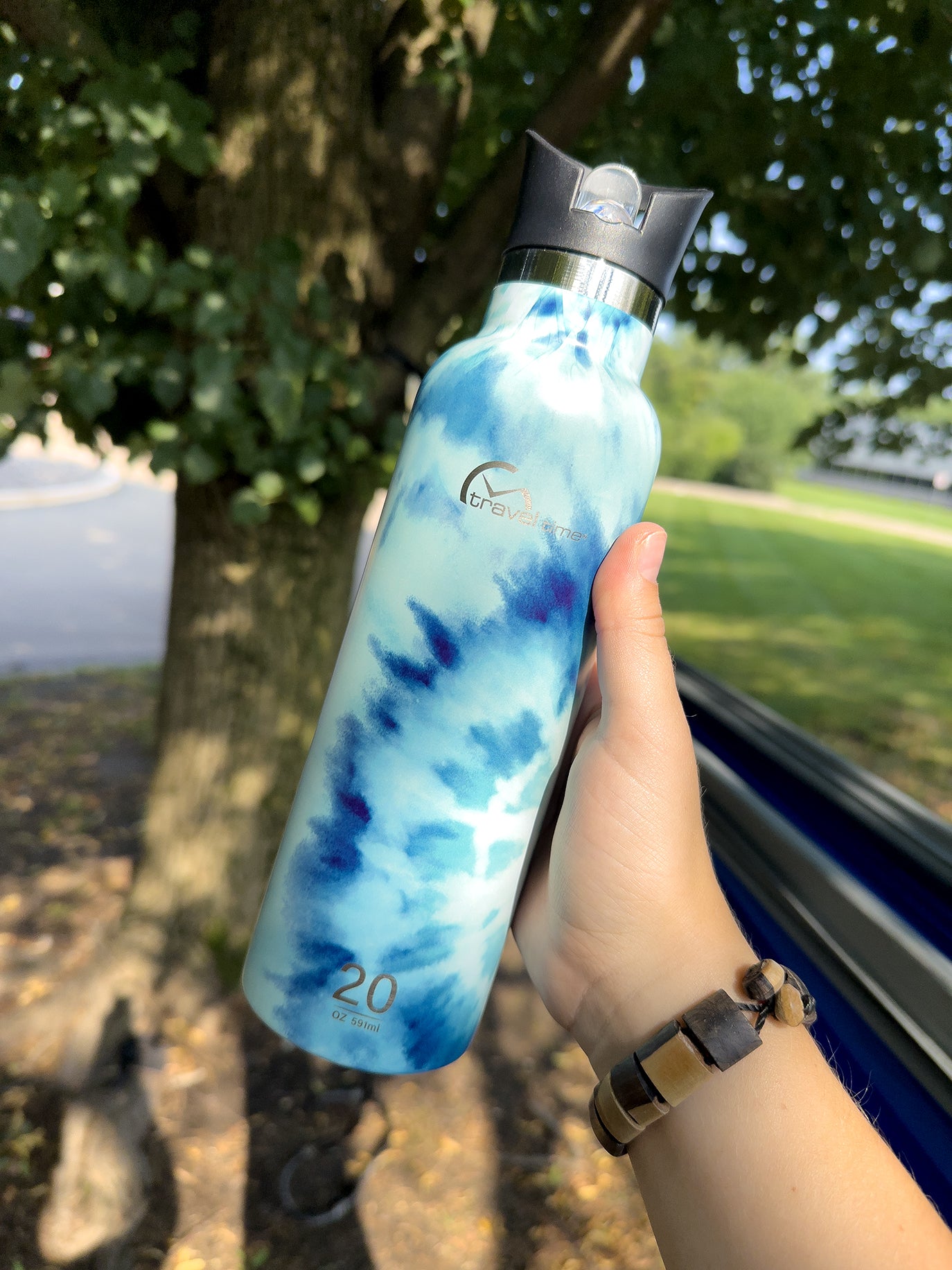 Stainless Steel Water Bottle with Flip Straw 20oz held in hand of someone who is outside camping in nature in front of a tree